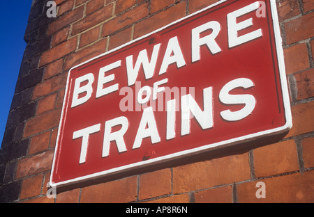 Bold metal sign peint en blanc sur rouge écarlate sur mur brique orange indiquant Attention aux trains avec ciel bleu profond Banque D'Images