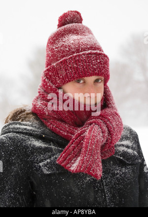 Une jeune femme portant un chapeau et un foulard rouge brave les éléments pendant une tempête d'hiver. Banque D'Images