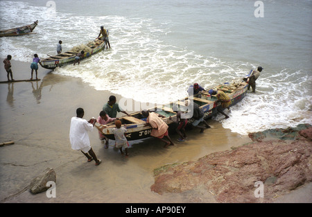 Les bateaux de pêche traditionnels en cours d'élaboration sur la plage de sable au pied des remparts du château de Cape Coast au Ghana Banque D'Images