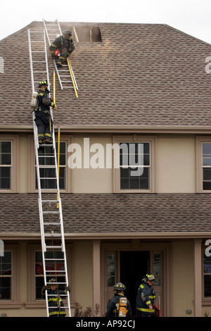 Les pompiers lors d'une scène d'incendie d'une maison qui était en feu des trous de ventilation ont été coupées Banque D'Images