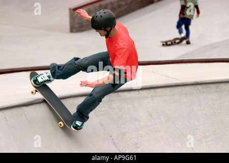 Une action d'arrêt image d'un jeune passionné de planche à roulettes à un skate park, avec une deuxième patineur dans l'arrière-plan. Banque D'Images