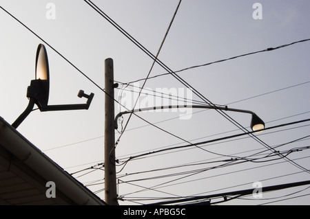 Enchevêtrement de fils haute une lampe de rue et d''une télévision par satellite plat sur le bord d'un toit avec ciel derrière à l'aube Banque D'Images