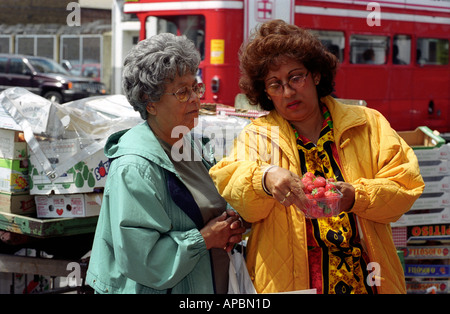 Deux femmes âgées l'examen de la qualité de la Fraise dans un marché à Peckham, Southwark, dans le sud de Londres, au Royaume-Uni. Banque D'Images