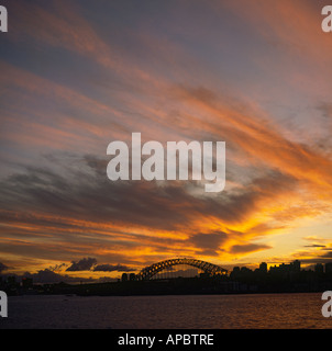 Fiery spectaculaire coucher de soleil de nuages striés orange avec Sydney Harbour Bridge et sur les toits de la ville en silhouette Sydney Australie Banque D'Images