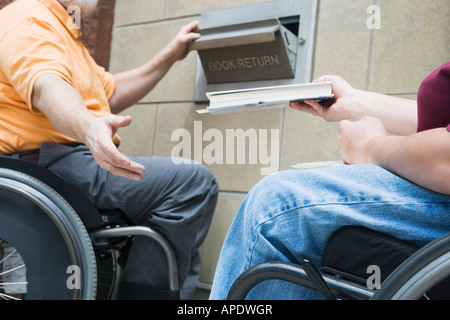 Couple en fauteuil roulant retour d'un livre dans un emplacement de la bibliothèque Banque D'Images