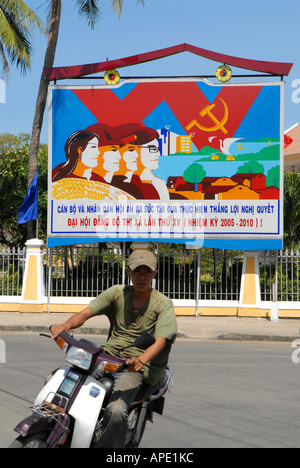 Moto passant devant une affiche socialiste dans la ville de Hoi An, Vietnam Banque D'Images