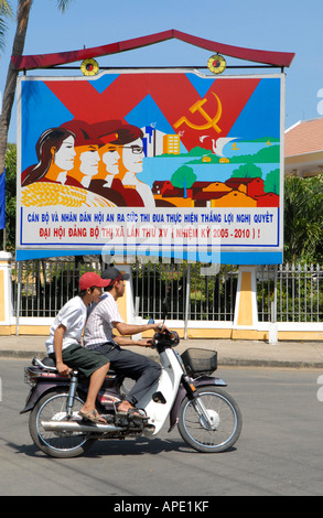 Moto passant devant une affiche socialiste dans la ville de Hoi An, Vietnam Banque D'Images
