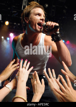 Low angle view of male rock star chanter sur scène avec adorant fans atteindre leurs mains jusqu'à lui Banque D'Images