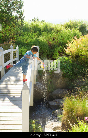 Asian boy verser de l'eau over bridge railing Banque D'Images