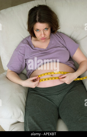 Femme enceinte, assise sur une chaise, la mesure de son ventre avec un ruban à mesurer. Parution du modèle. Banque D'Images