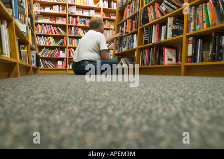 Homme assis sur le sol dans une librairie, à la recherche à travers les livres dans une bibliothèque. Banque D'Images