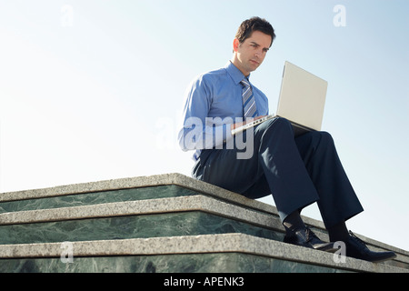 Young business man sitting on en plate-forme, à l'aide d'ordinateur portable. Banque D'Images