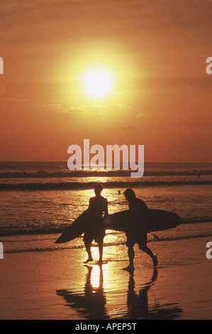 Deux surfers silhouetted par le coucher de soleil sur la plage de Kuta à Bali Banque D'Images