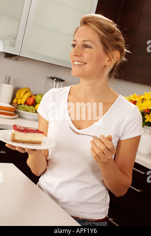 Femme dans la cuisine manger du gâteau au fromage Banque D'Images