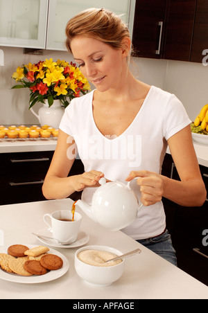 WOMAN IN KITCHEN POURING TEA Banque D'Images