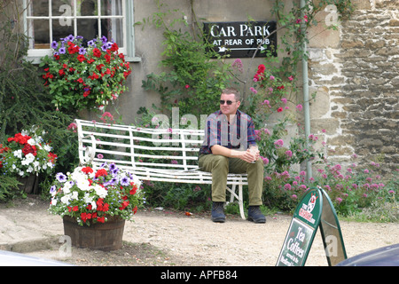 Un buveur solitaire sur un banc à l'extérieur d'un pub à Lacock, Banque D'Images