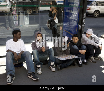 Les adolescents s'asseoir sur le trottoir à un arrêt de bus à Manhattan après l'école Banque D'Images