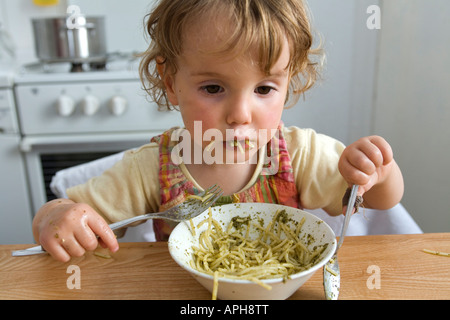 Une jeune fille de manger des pâtes au pesto à la table de la cuisine. Banque D'Images