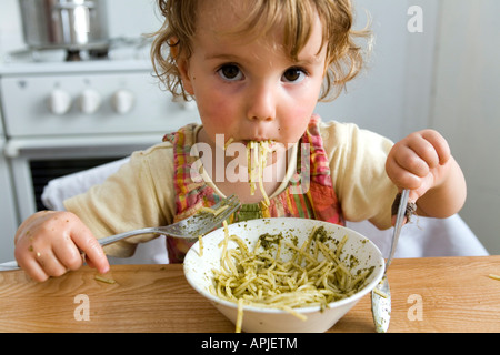 Une jeune fille de manger des pâtes au pesto à la table de la cuisine. Banque D'Images