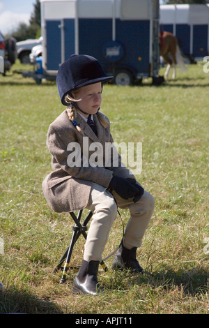 Petite fille âgée de huit EN TENUE D'ÉQUITATION AU PONEY CLUB EN ATTENTE D'UNE RIDE UK Banque D'Images