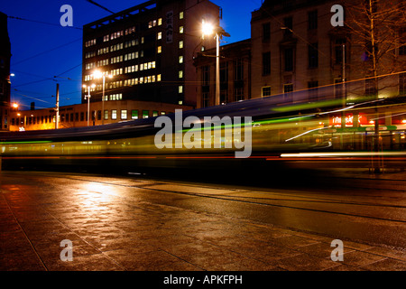 Le trouble d'un tramway à Nottingham la nuit à Nottinghams Place du marché. Lumières des boutiques locales et l'éclairage des rues de transformer l'apparence de Nottinghams Place du marché. Les piétons apparaissent comme de simples taches floues en raison de la longue exposition requis pour cette image. Place du marché, Nottingham, Royaume-Uni Banque D'Images