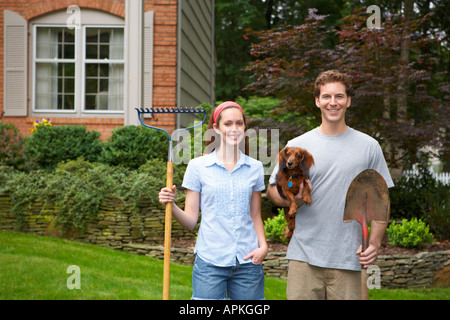 Young couple holding dog et outils de jardin Banque D'Images