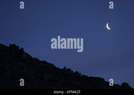 Croissant de lune au-dessus de la ligne de crête qui se profile dans le ciel nocturne clair Banque D'Images