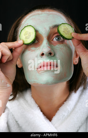 Brunette woman épluche des tranches de concombre sur ses paupières pendant un avocat pack visage séance de traitement du visage Banque D'Images