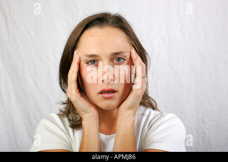 Jeune femme brune à la choqué stupéfié surpris incrédules confus se tenant la main jusqu'à son visage tshirt blanc Banque D'Images