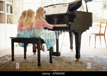 Des triplés à jouer du piano dans la salle de séjour (vue arrière) Banque D'Images