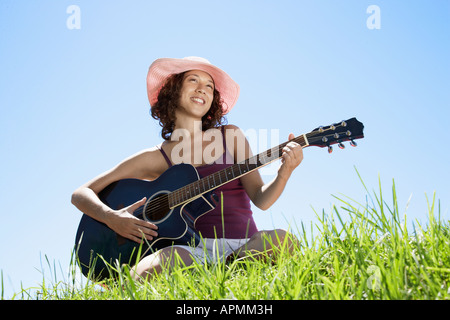 Jeune femme jouant de la guitare sur l'herbe (low angle view) Banque D'Images