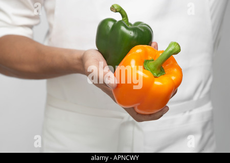 Chef holding deux paprikas (mid section) Banque D'Images