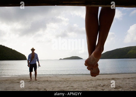 Mid adult man standing on beach, les jambes de la femme en premier plan, St John, US Virgin Islands, USA Banque D'Images