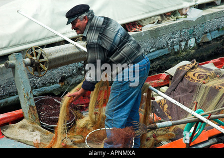 Un pêcheur travaille sur ses filets sur un petit bateau de pêche traditionnel grec Banque D'Images