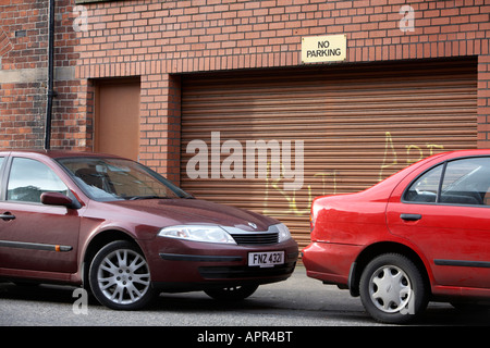 Deux voitures garées en face de garage en acier avec obturateur no parking sign Belfast Irlande du Nord UK Banque D'Images