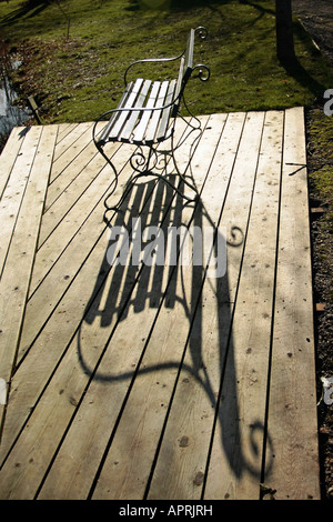 Siège de jardin en fer forgé jetant l'ombre sur la terrasse en bois fin d'hiver. Sussex, Angleterre, Royaume-Uni Banque D'Images