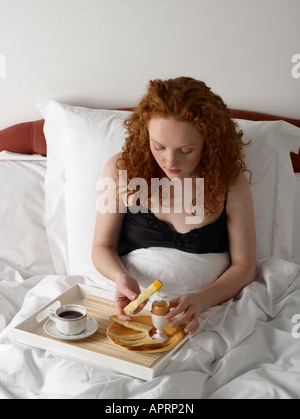 Jeune femme ayant le petit déjeuner au lit oeuf dur avec le pain blanc soldats tasse de café noir Banque D'Images