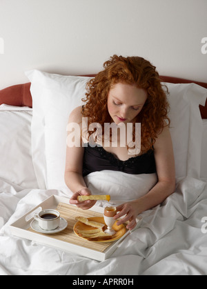 Jeune femme ayant le petit déjeuner au lit oeuf dur avec le pain blanc soldats tasse de café noir Banque D'Images