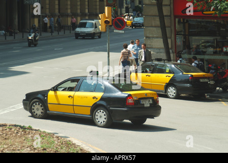 Vue latérale et arrière de Barcelone deux taxis et piétons noirs et jaunes emblématiques dans la circulation espagnole animée scène de rue Catalogne Espagne UE Banque D'Images