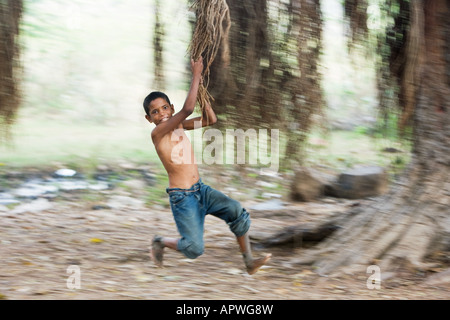 Jeune Indien se balancer les racines aériennes d'un banian dans la campagne. L'Andhra Pradesh, Inde Banque D'Images