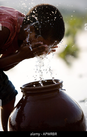 Village de l'Inde rurale garçon laver le visage d'un pot en argile à côté d'un champ de riz. L'Andhra Pradesh, Inde Banque D'Images