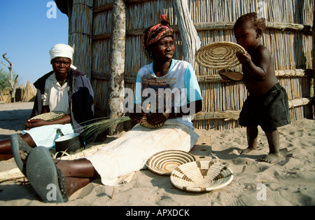 Femme tissant un Botswana traditionnel panier avec un jeune enfant tenant une des baskets Banque D'Images