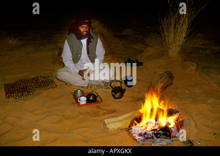 Homme touareg assis près d'un feu avec des petits pots pour faire du thé en face de lui sur un plateau Banque D'Images