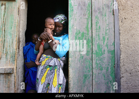 Jeune mère tenant un bébé dans l'entrée dans un village le long du fleuve Niger Banque D'Images