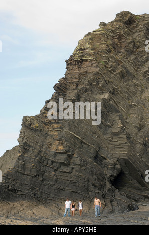 Quatre jeunes personnes marchant sur la côte rocheuse au-dessous des falaises le montrant les strates de roche Ceredigion Aberystwyth Wales UK Banque D'Images