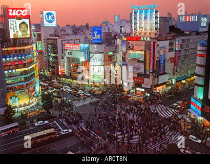 Les piétons aux passages pour piétons de remplissage à Shibuya district de Tokyo sous le coucher du soleil ciel dégagé et néons de façades de grande hauteur Banque D'Images