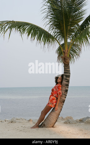 Young woman leaning against palm tree. Banque D'Images