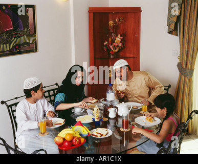 Femme met du beurre sur le pain tandis que son mari et ses enfants qui la regardent, pendant le petit déjeuner. Banque D'Images