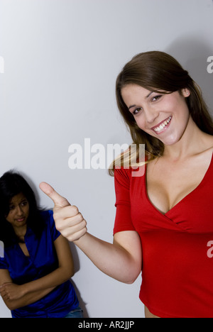 Deux jeunes femmes, l'un souriant de pouce vers le haut tandis que l'autre est déçu derrière Banque D'Images