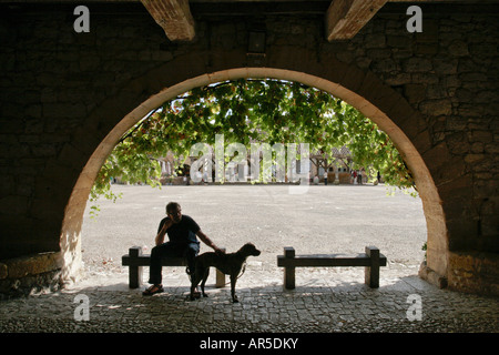 Silhouette d'un homme avec chien assis sous une voûte en pierre médiévale dans la ville Bastide de Monpazier en Dodogne, France Banque D'Images